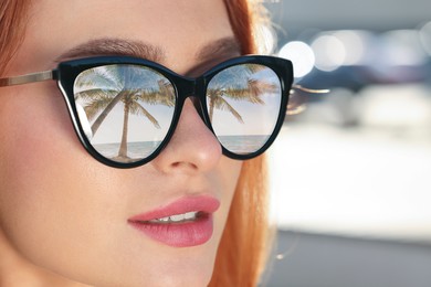 Beautiful woman in sunglasses on sunny day outdoors. Beach with palm tree reflecting in lenses