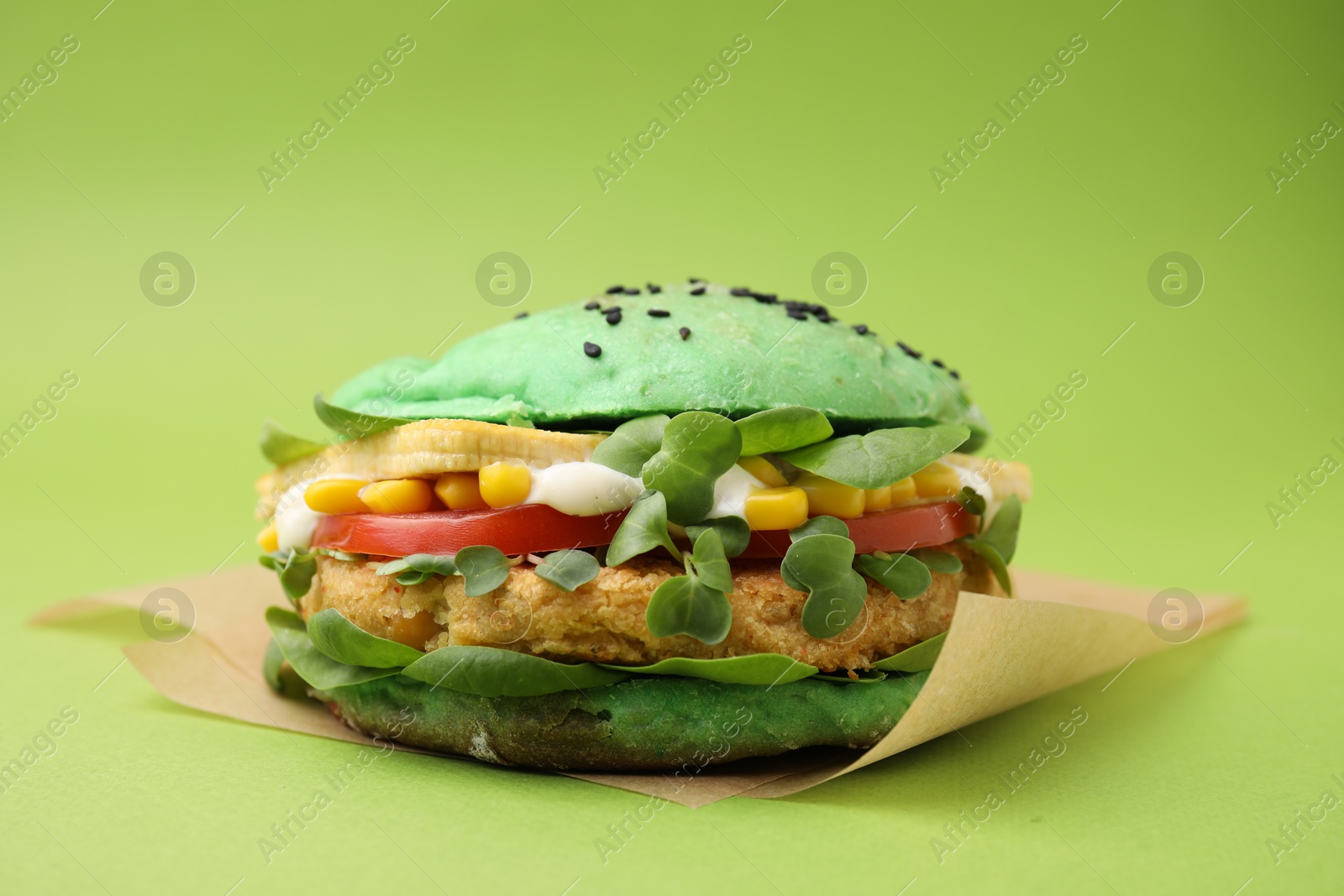 Photo of Tasty vegan burger with vegetables, patty and microgreens on green background, closeup