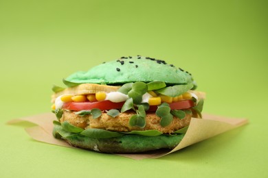 Tasty vegan burger with vegetables, patty and microgreens on green background, closeup