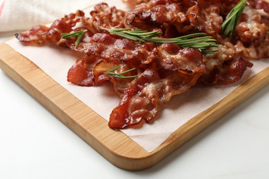 Photo of Slices of tasty fried bacon with rosemary on white table, closeup