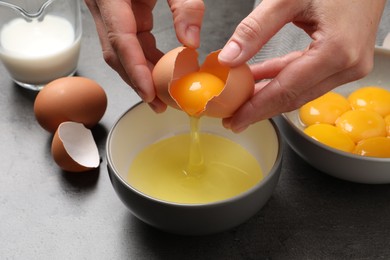 Photo of Woman separating egg yolk from white over bowl at grey table, closeup