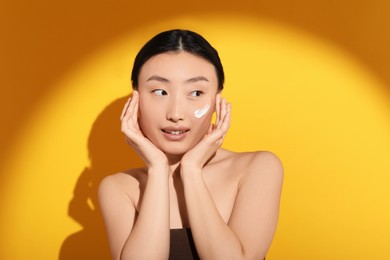 Photo of Beautiful young woman in sunlight with sun protection cream on her face against orange background