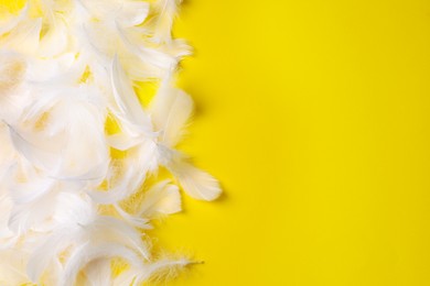 Photo of Many fluffy bird feathers on yellow background, flat lay. Space for text