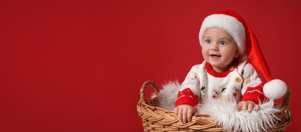Image of Cute baby in wicker basket on red background, banner design with space for text. Christmas celebration