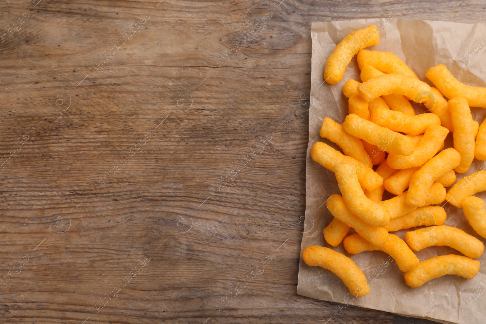 Photo of Many tasty cheesy corn puffs on wooden table, top view. Space for text