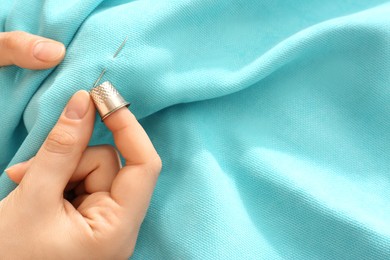 Photo of Woman sewing on turquoise fabric with thimble and needle, above view. Space for text