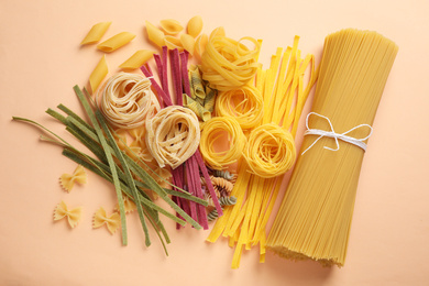 Photo of Different types of pasta on light orange background, flat lay