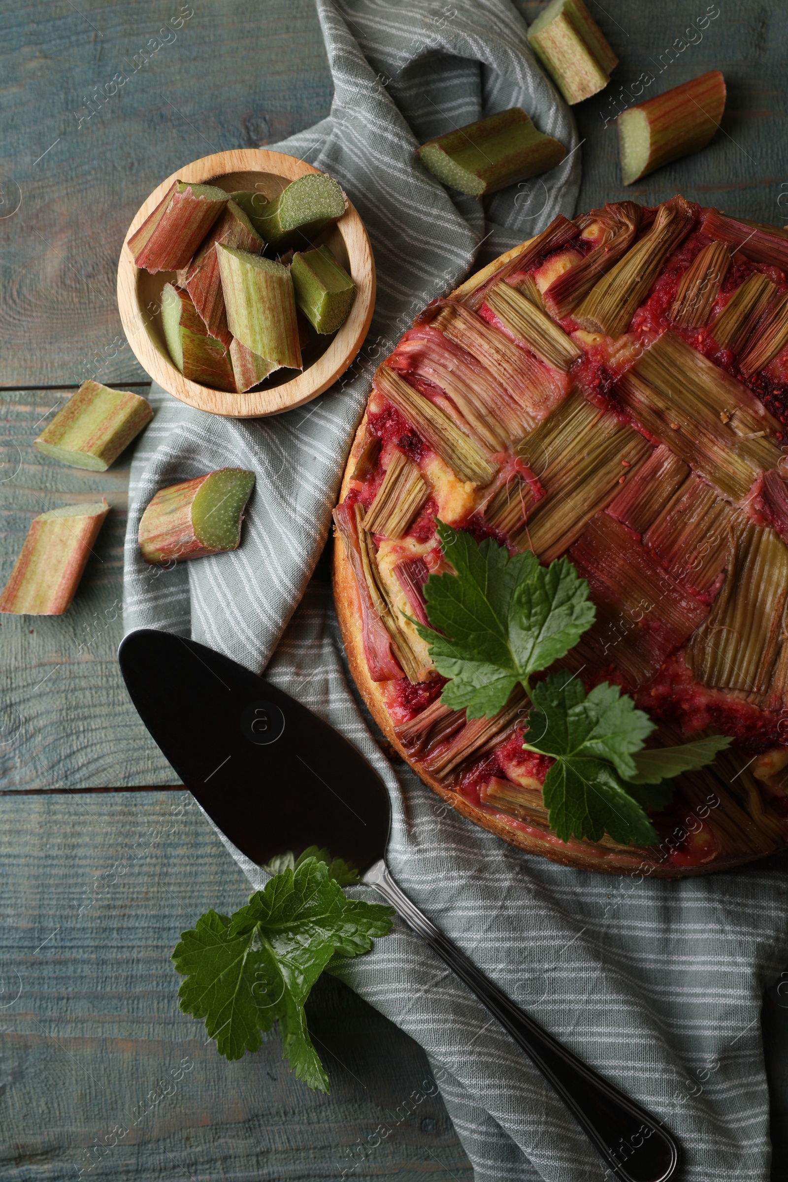 Photo of Freshly baked rhubarb pie, cut stalks and cake server on wooden table, flat lay