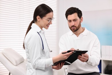 Photo of Doctor with clipboard consulting patient during appointment in clinic