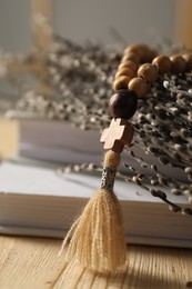 Rosary beads, books and willow branches on table, closeup