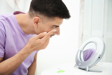 Young man putting contact lens in his eye indoors