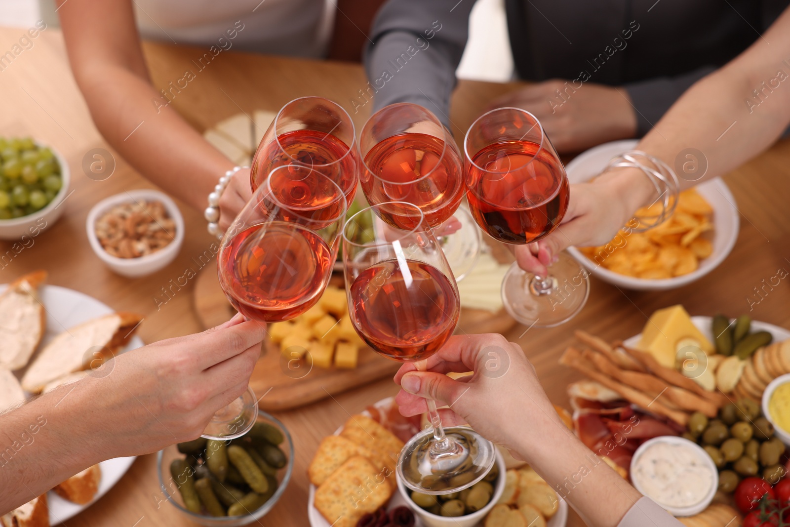 Photo of People clinking glasses with rose wine above wooden table, closeup