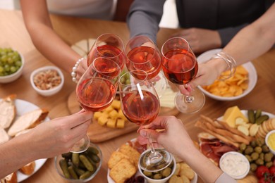 People clinking glasses with rose wine above wooden table, closeup