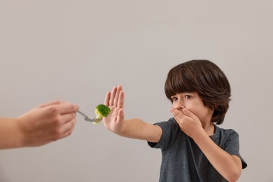 Photo of Cute little boy covering mouth and refusing to eat broccoli on grey background