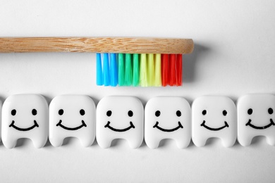 Photo of Small plastic teeth with happy faces and wooden brush on white background, top view