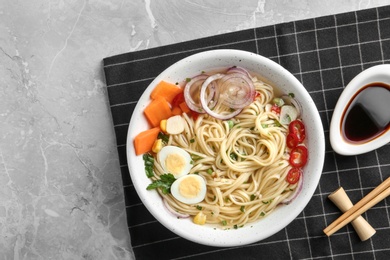 Photo of Bowl of noodles with broth, egg, vegetables and chopsticks served on table, flat lay