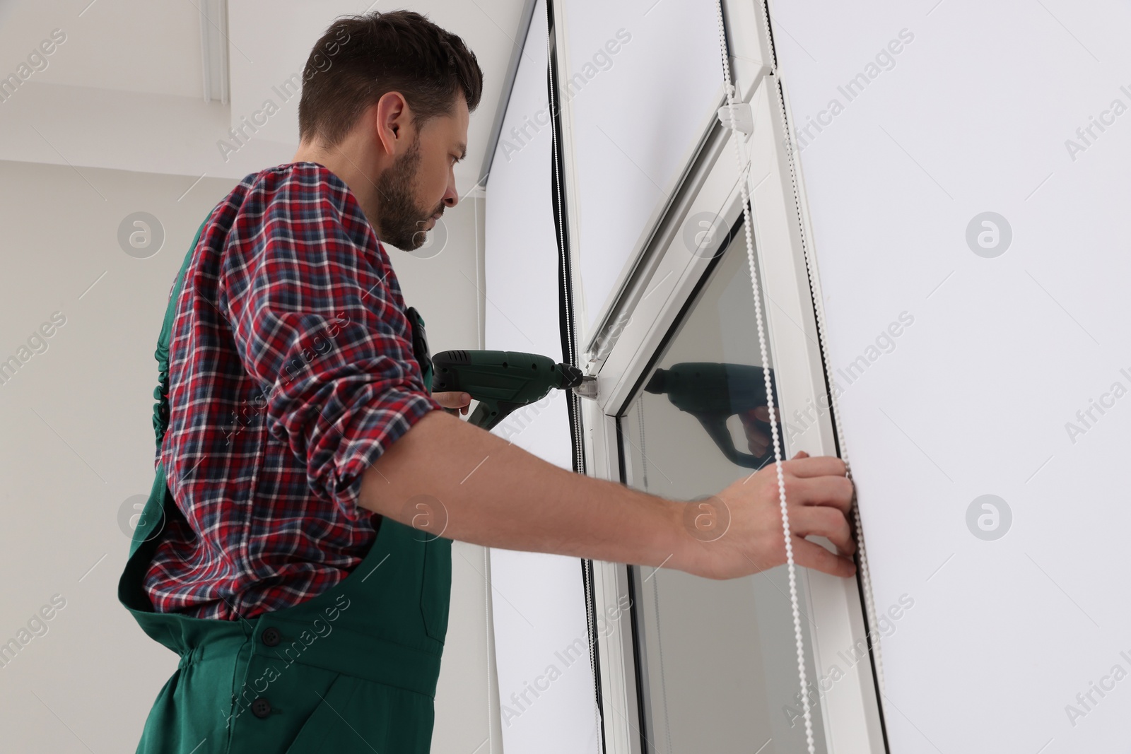 Photo of Worker in uniform installing roller window blind indoors