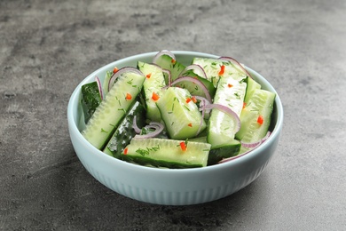 Photo of Delicious cucumber salad with onion in bowl on grey background