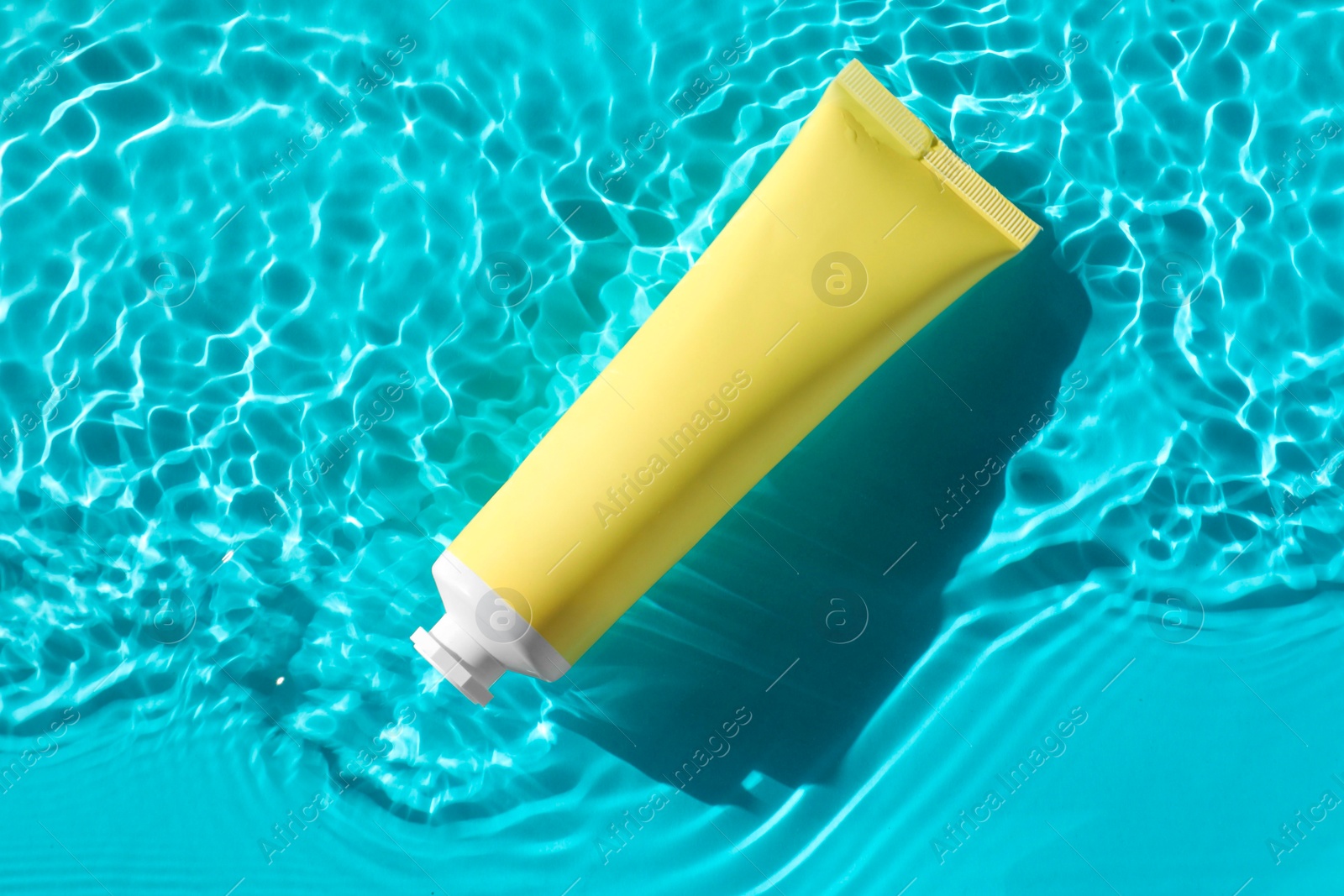 Photo of Tube with moisturizing cream in water on light blue background, top view