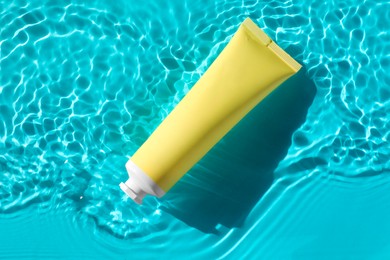 Photo of Tube with moisturizing cream in water on light blue background, top view