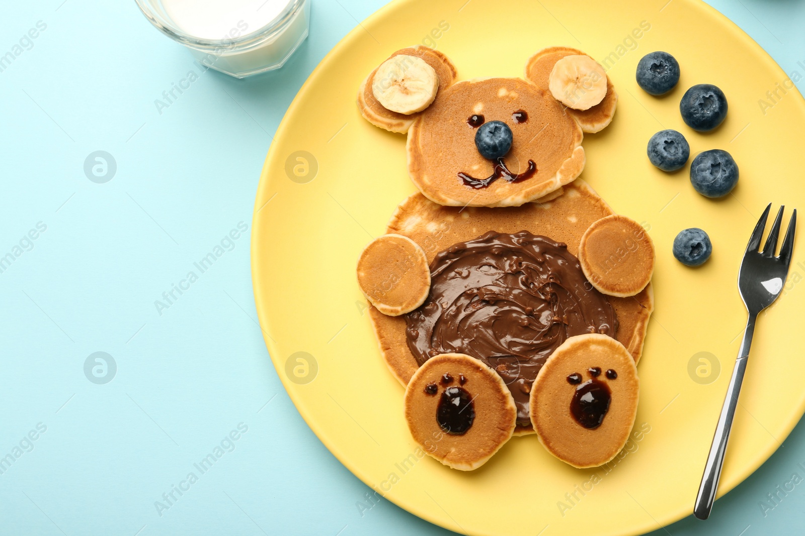 Photo of Creative serving for kids. Plate with cute bear made of pancakes, blueberries, bananas and chocolate paste on light blue table, top view. Space for text