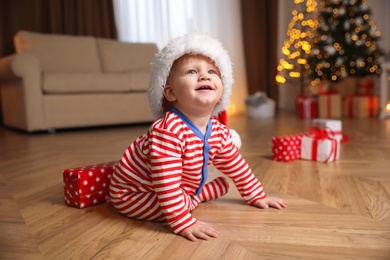Photo of Baby in Christmas pajamas and Santa hat near gift box  indoors