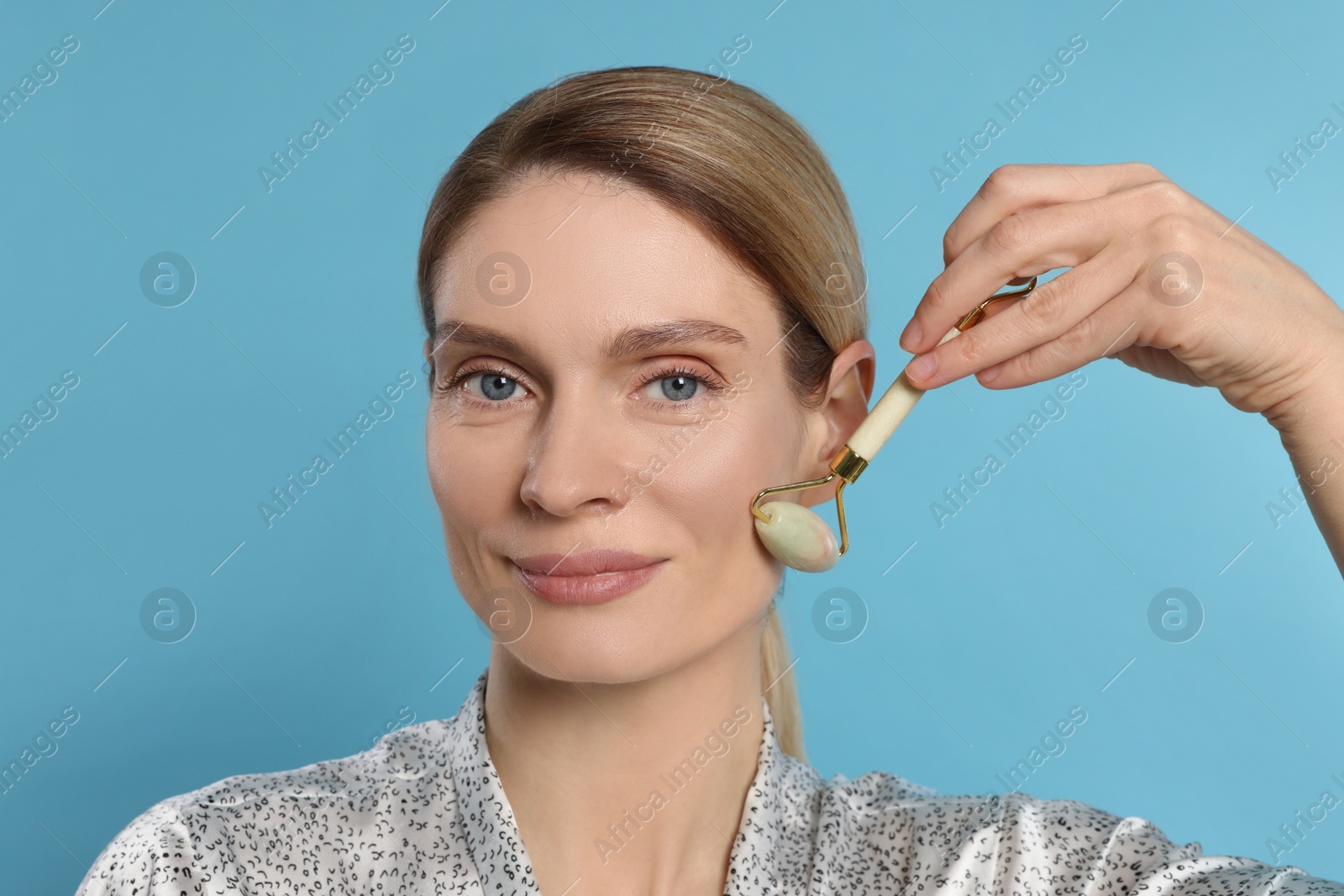 Photo of Woman massaging her face with jade roller on turquoise background