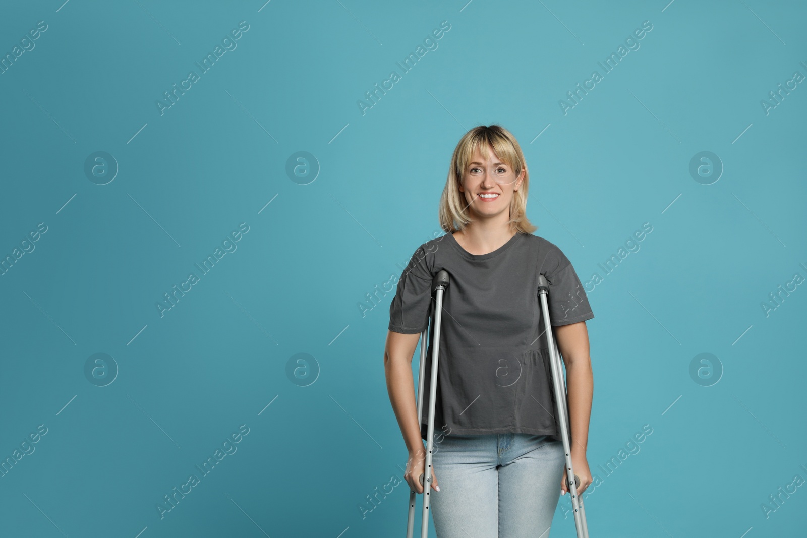 Photo of Portrait of happy woman with crutches on light blue background. Space for text