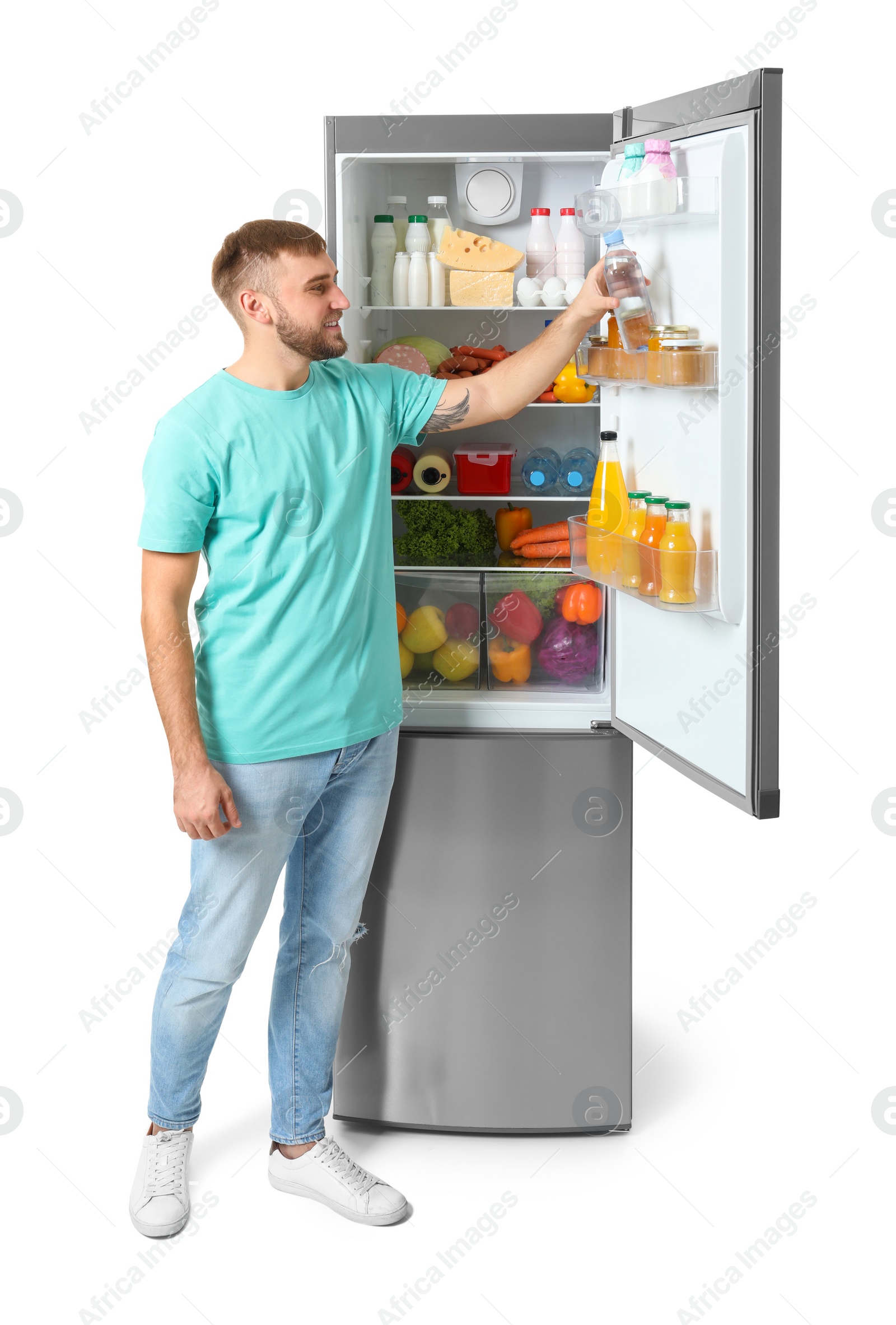 Photo of Young man taking bottle of water from refrigerator on white background