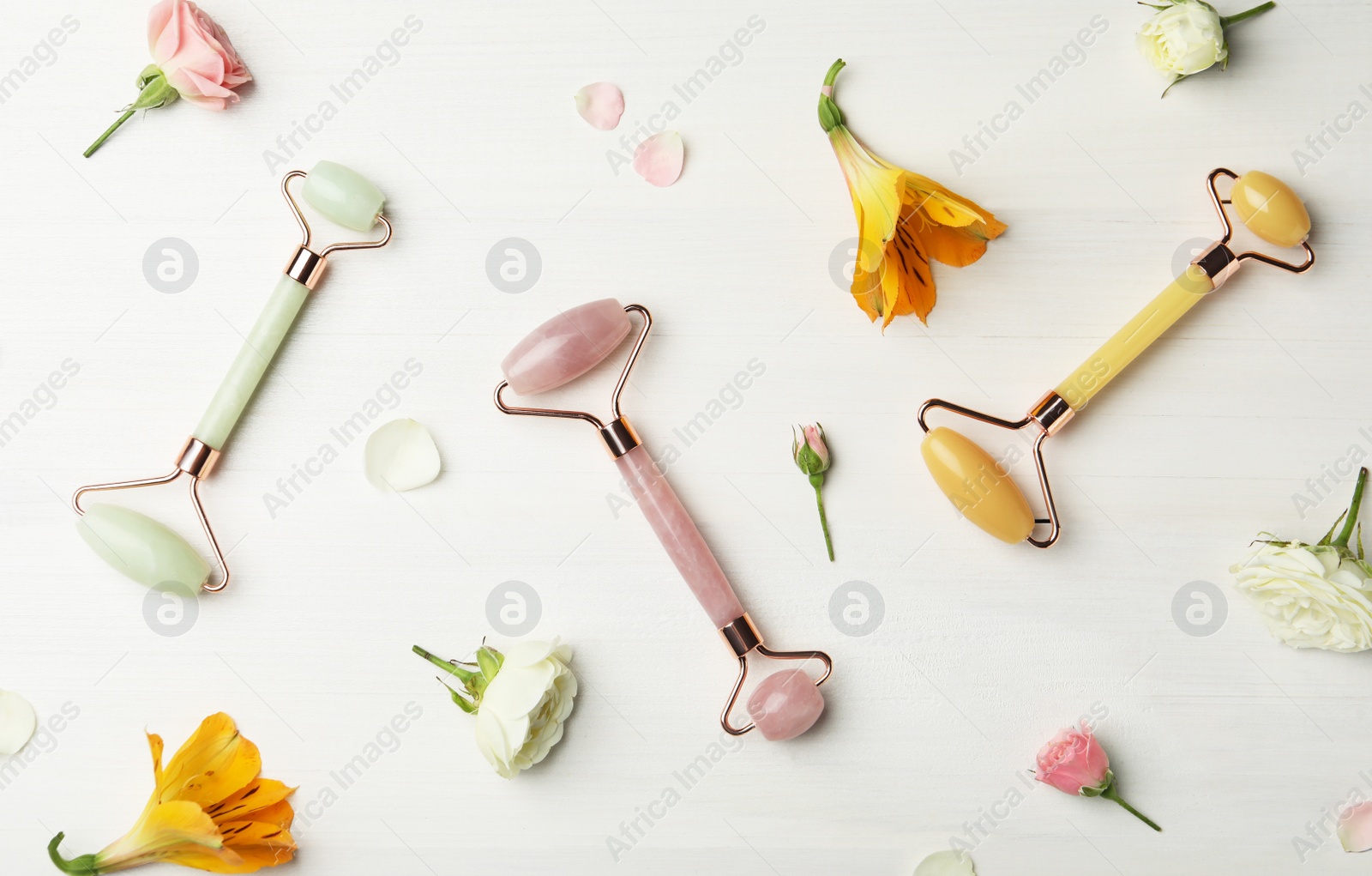 Photo of Different natural face rollers and flowers on white wooden background, flat lay