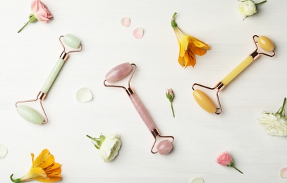 Photo of Different natural face rollers and flowers on white wooden background, flat lay
