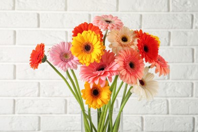 Photo of Bouquet of beautiful colorful gerbera flowers in vase against white brick wall