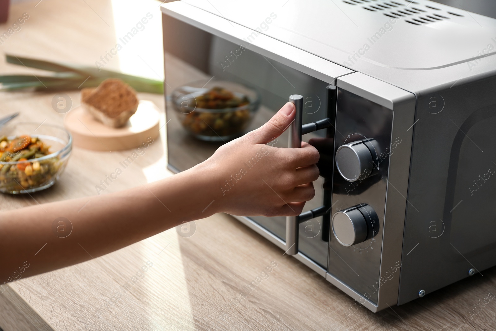 Photo of Young woman using microwave oven on table in kitchen