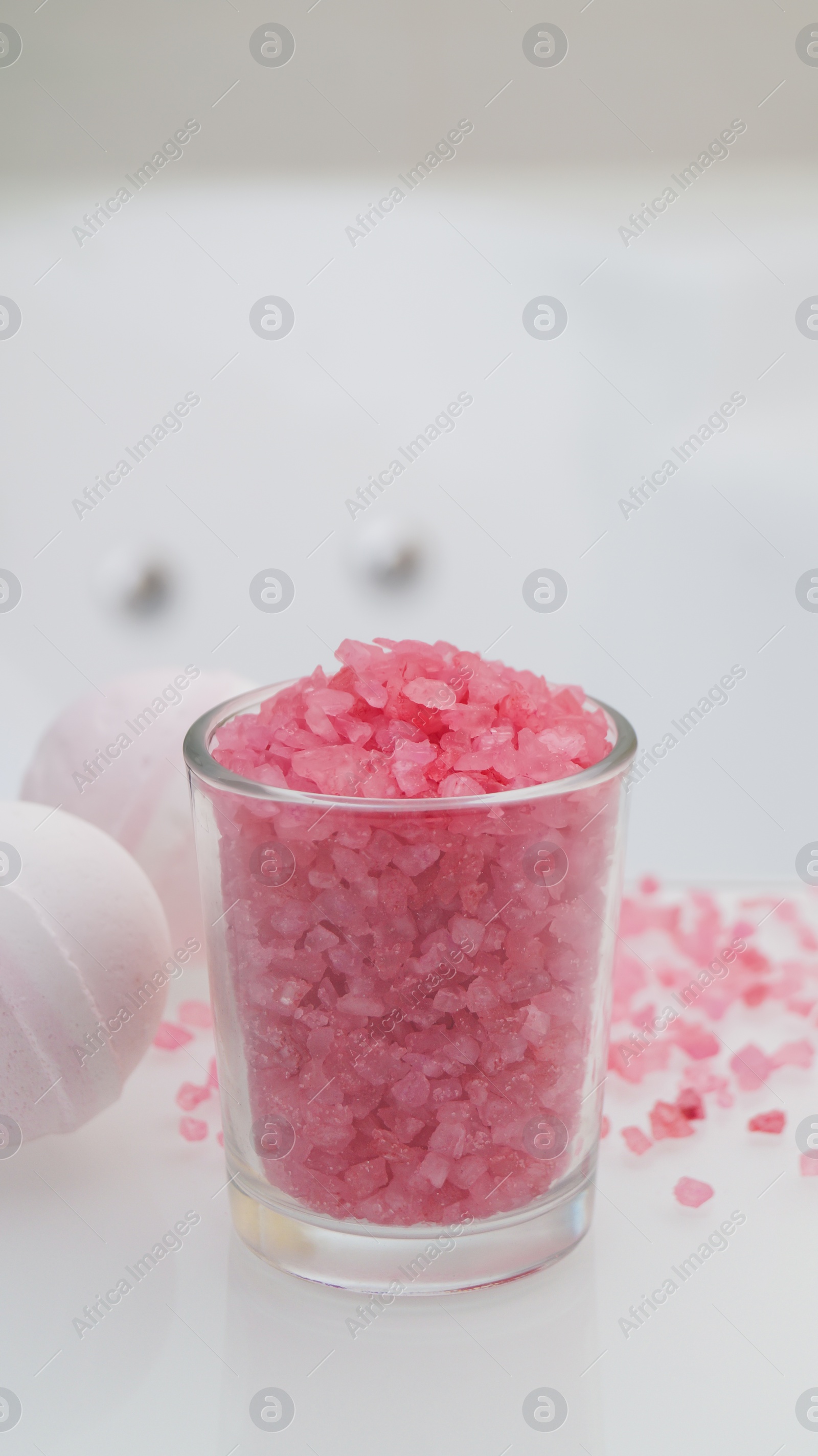Glass with sea salt and bath bombs on table in bathroom Photo of Glass with sea salt and bath bombs on table in bathroom