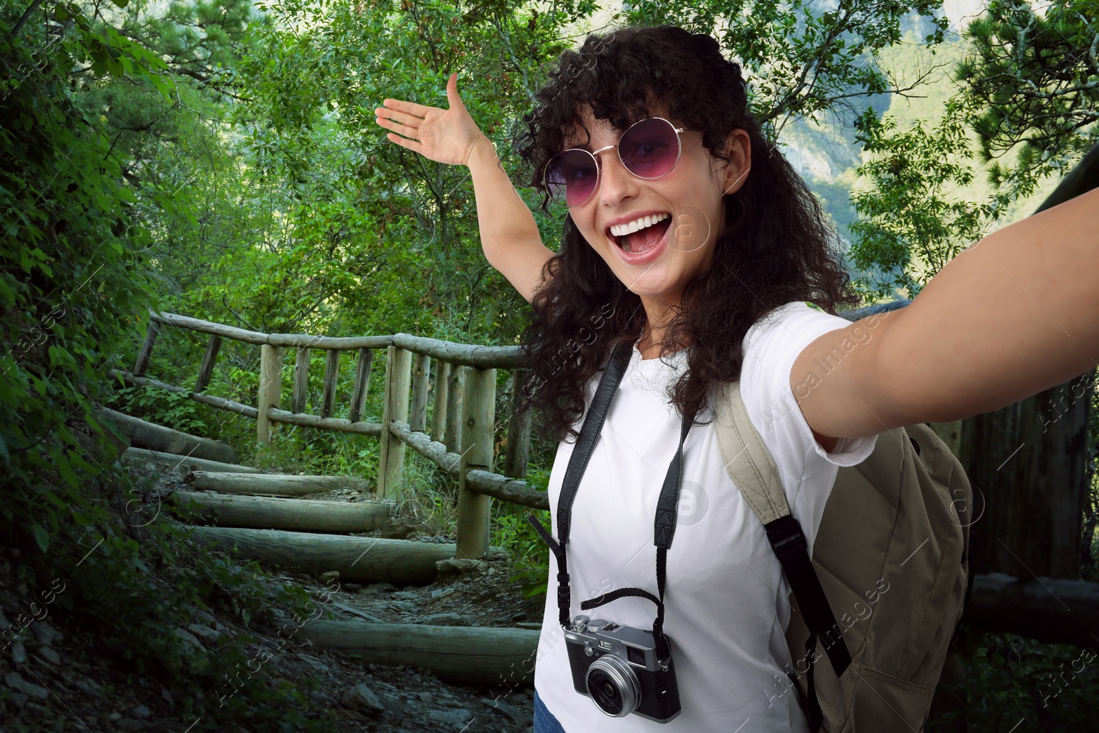Image of Beautiful woman in sunglasses with camera taking selfie on stairs in mountains