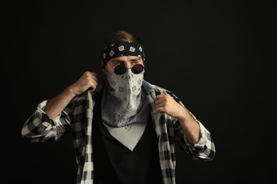 Fashionable young man with bandana covering his face on black background