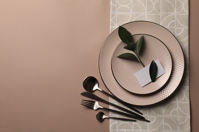 Stylish table setting. Plates, cutlery, blank card and green twig on beige background, top view with space for text