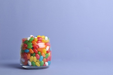 Photo of Glass jar with delicious bright jelly beans on color background. Space for text