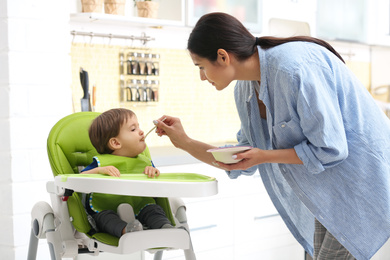 Photo of Young nanny feeding cute little baby in kitchen