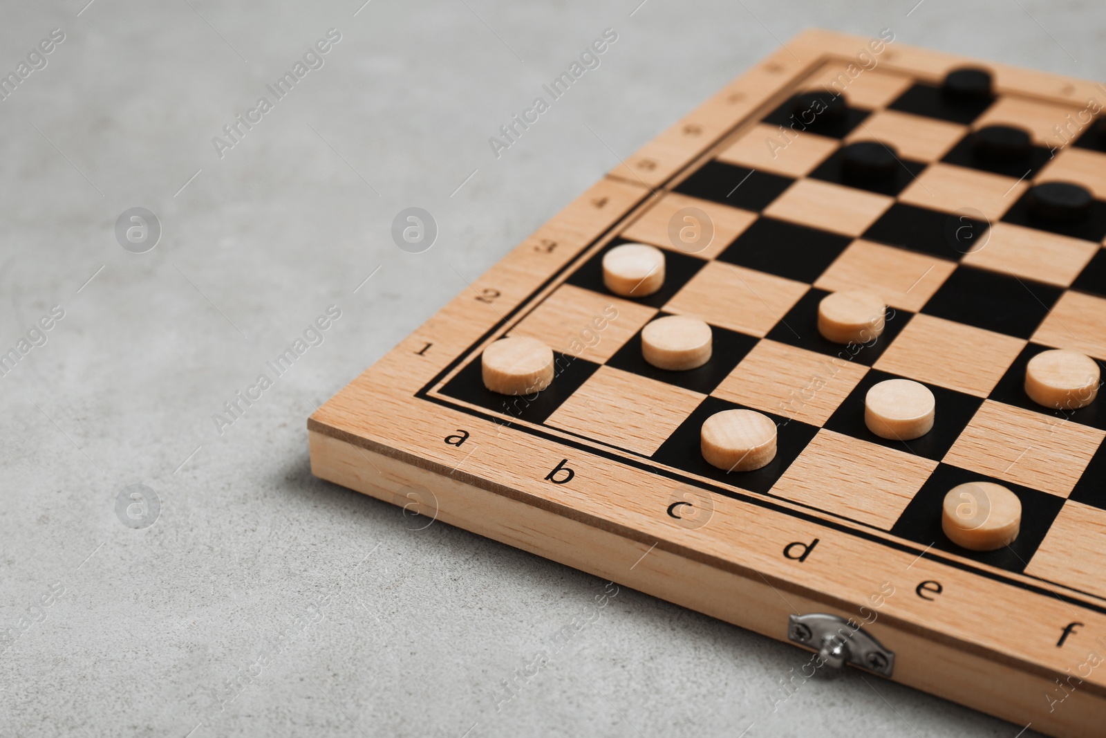 Photo of Wooden checkerboard with game pieces on light grey table, closeup. Space for text