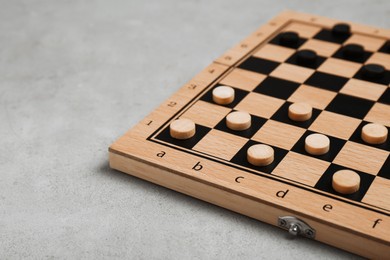 Photo of Wooden checkerboard with game pieces on light grey table, closeup. Space for text