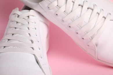 Pair of stylish white sneakers on pink background, closeup