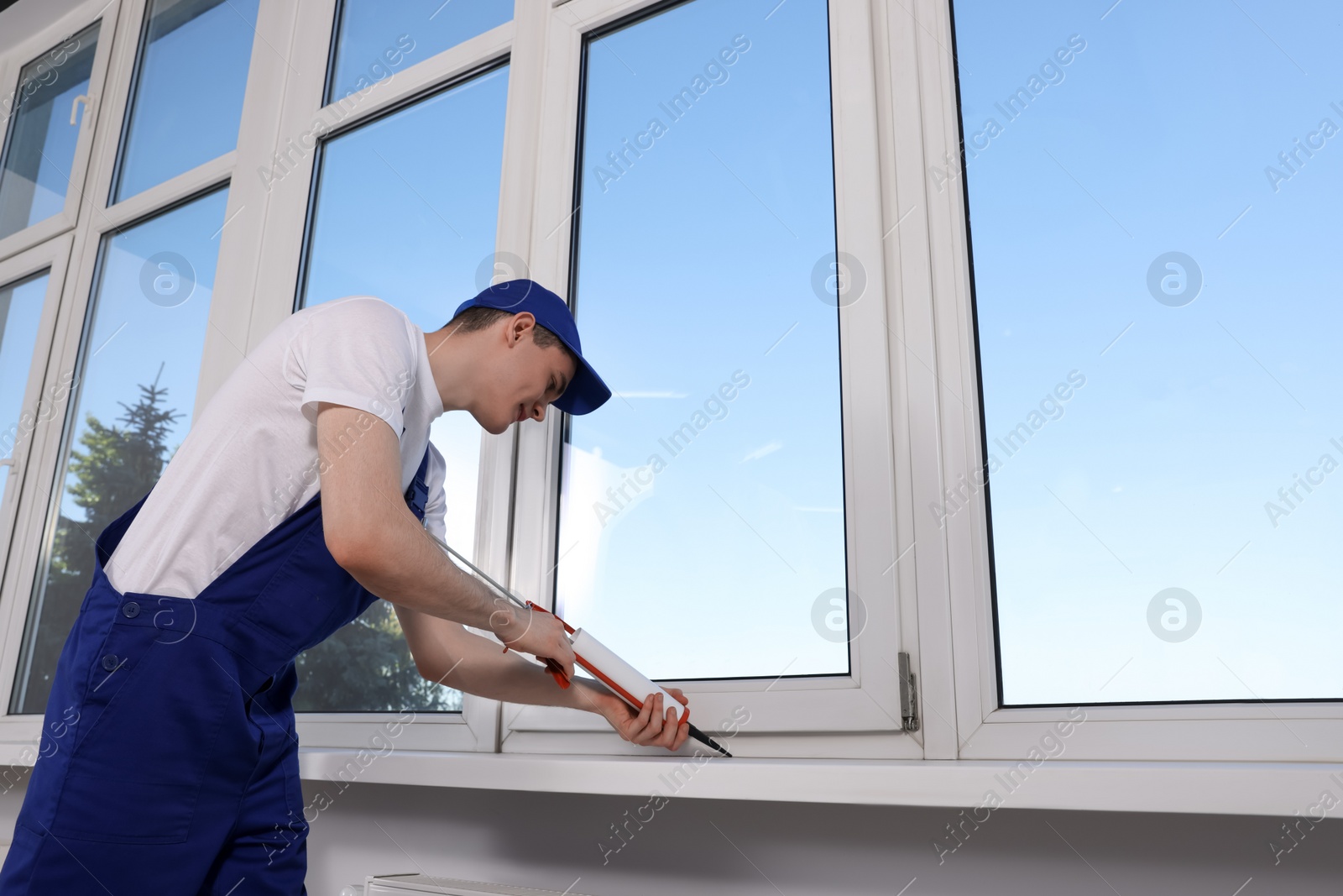 Photo of Worker sealing plastic window with caulk indoors. Installation process