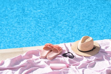Photo of Pink blanket with slippers, hat, sunglasses and sunscreen near outdoor swimming pool on sunny day, space for text