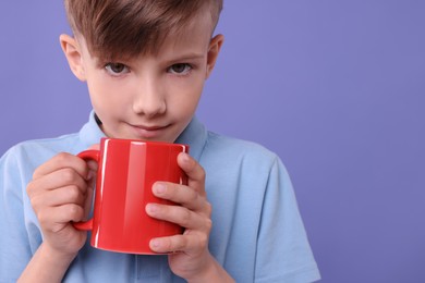 Photo of Cute boy with red ceramic mug on violet background, space for text