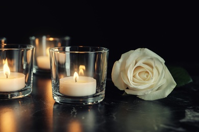 White rose and burning candles on table in darkness. Funeral symbol