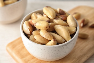 Bowl with tasty Brazil nuts on wooden board