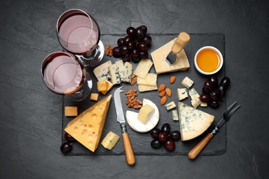 Photo of Cheese platter with specialized knife and fork on black table, flat lay