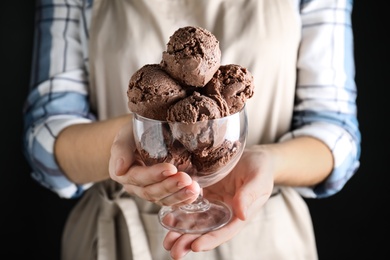 Photo of Woman holding glass bowl full of chocolate ice cream on black background, closeup