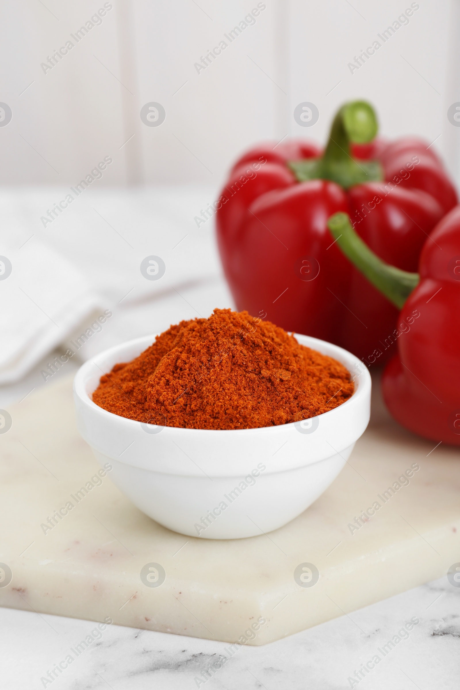 Photo of Bowl with aromatic paprika powder and fresh bell peppers on white marble table